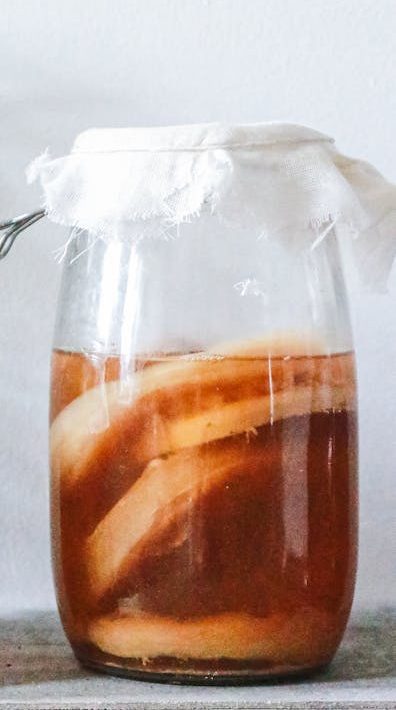 Close-up of kombucha brewing in jars with a rustic setting, showcasing natural fermentation process.