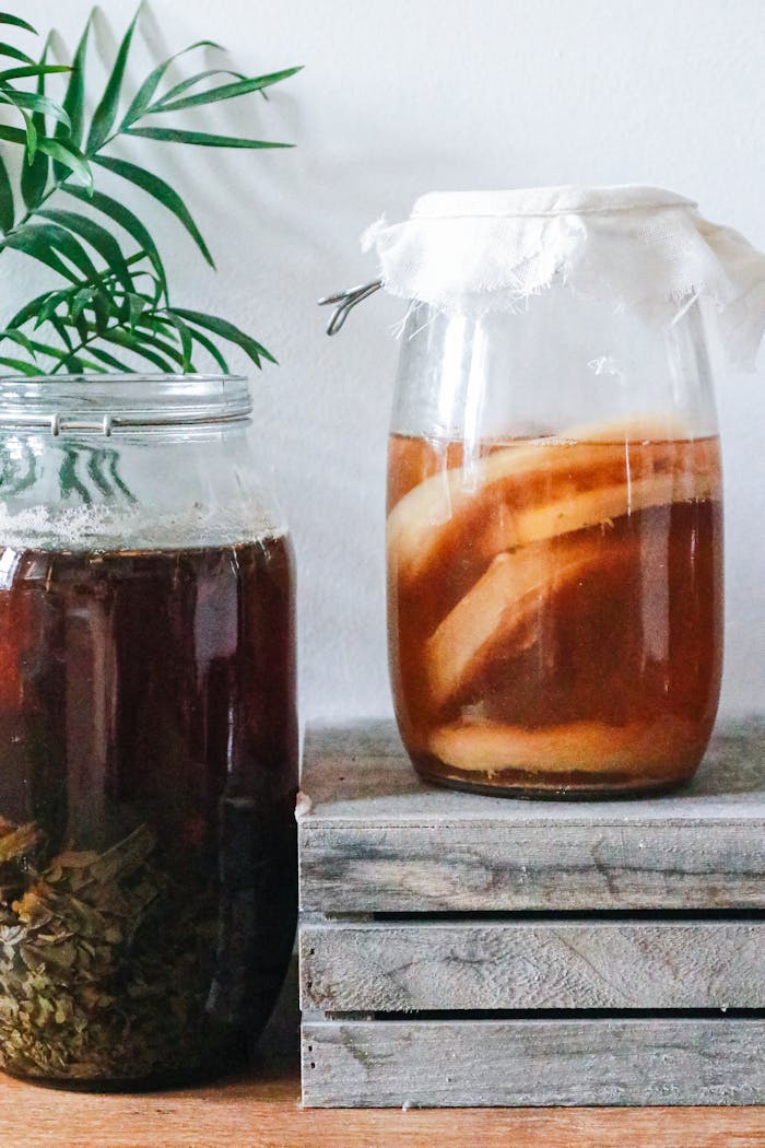 hero-img-02 Close-up of kombucha brewing in jars with a rustic setting, showcasing natural fermentation process.