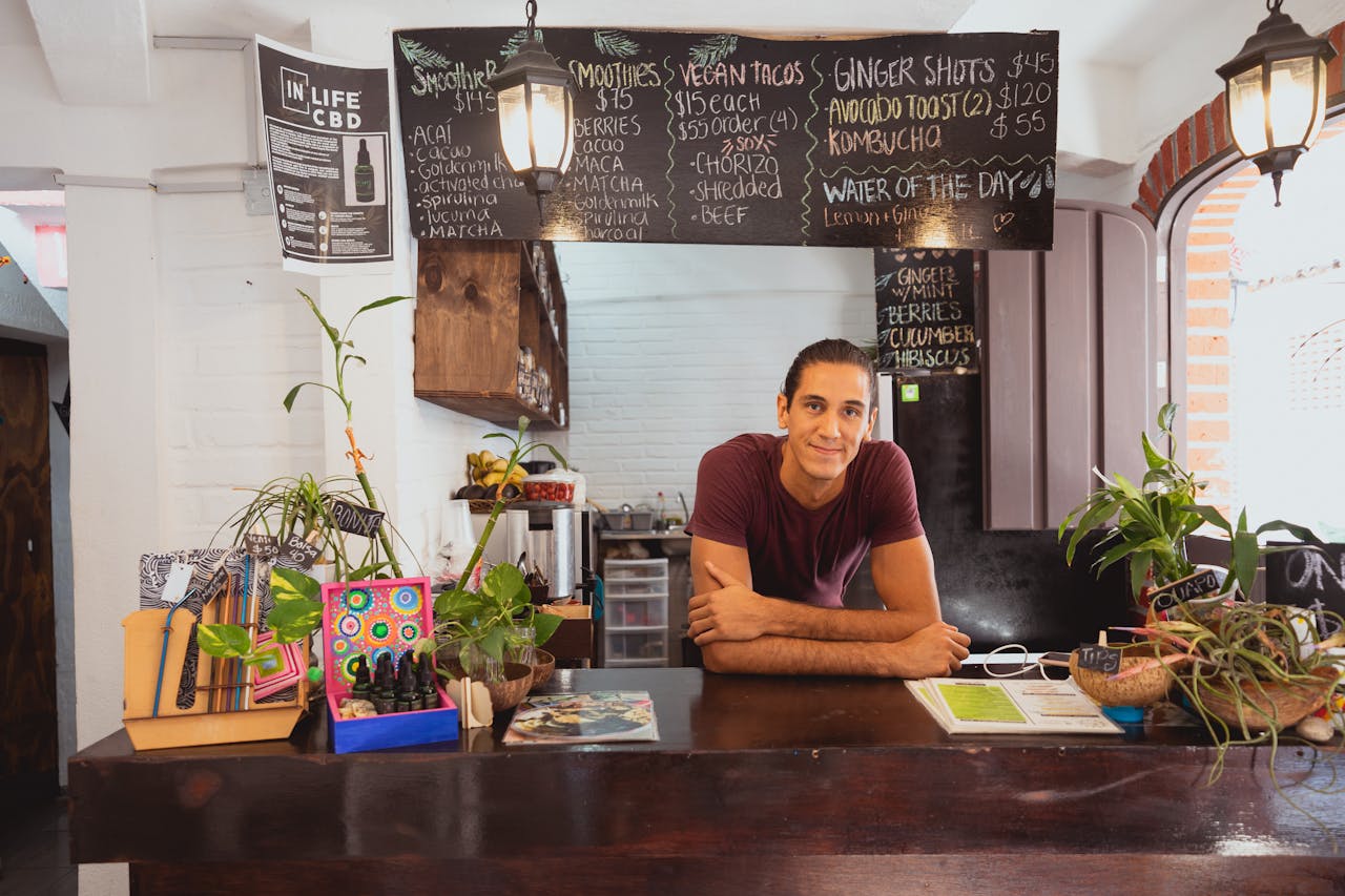 our-services-1 Cozy cafe scene featuring a friendly barista behind the counter with a menu board and potted plants.